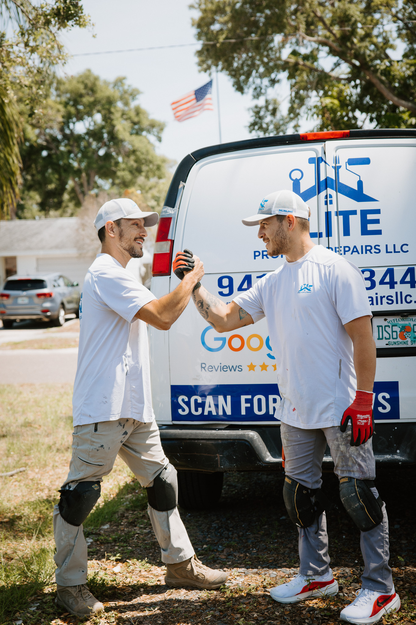 Elite Property Repairs crew fist-bumping at their work van on a job site in St. Petersburg FL — home services photography by Orange Grove Social